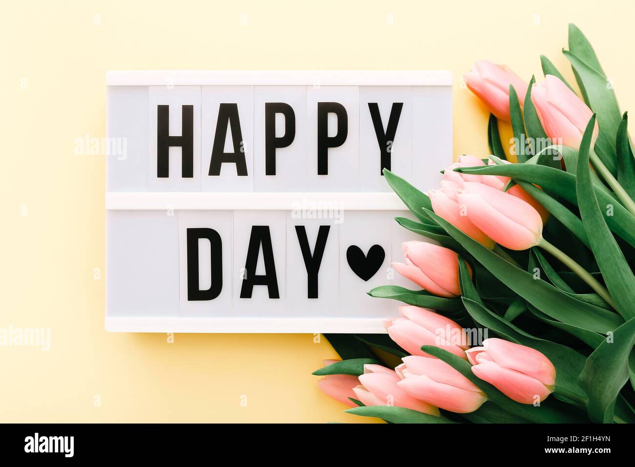Happy Day parole sulla scatola luminosa con bouquet di tulipani rosa su sfondo giallo chiaro. Foto Stock