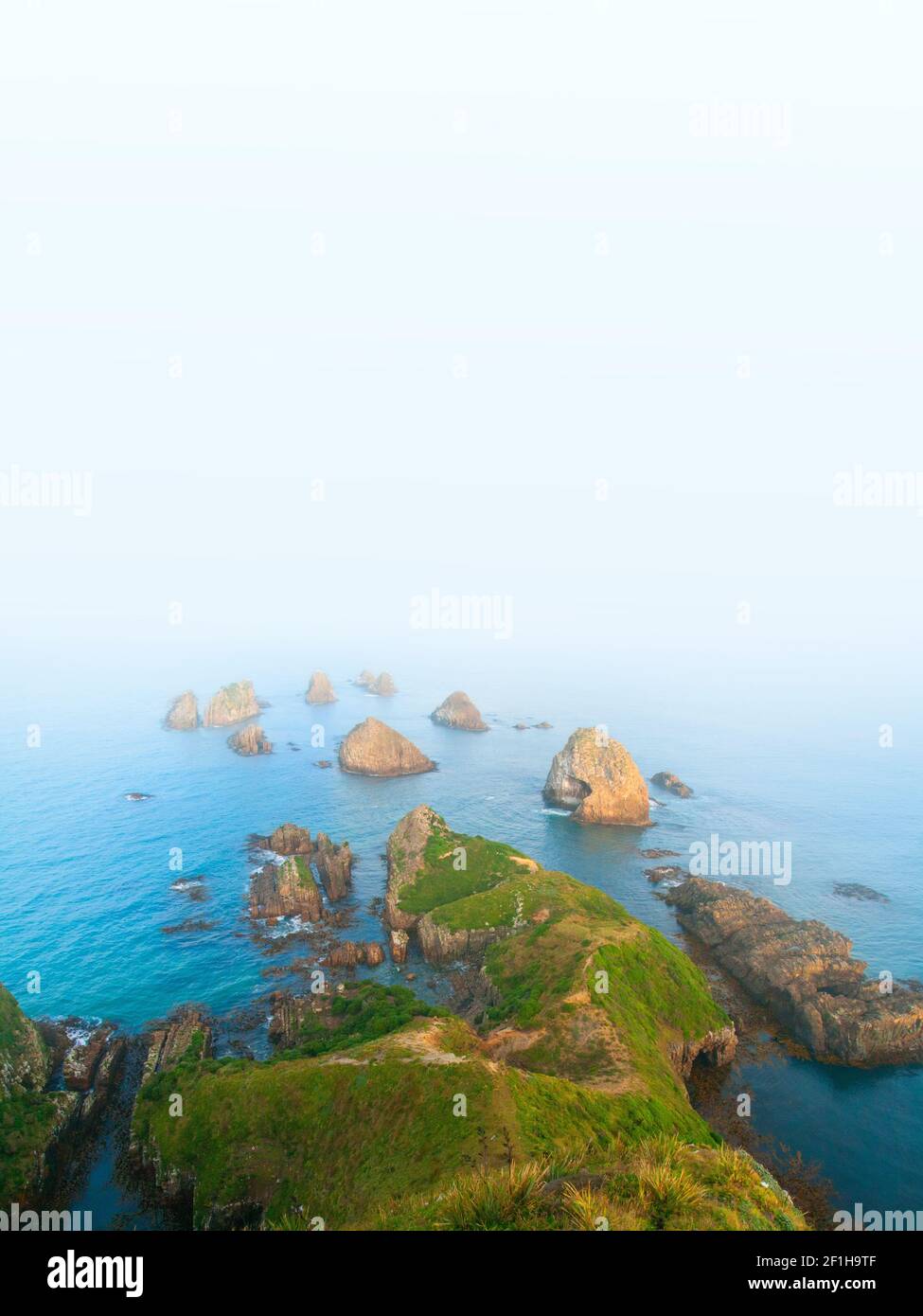 I pappagagli, iconici isolotti rocciosi di Nugget Point scomparendo nell'infinita nebbia bianca astratta dell'Oceano Pacifico meridionale, la costa di Catlins, a sud Foto Stock