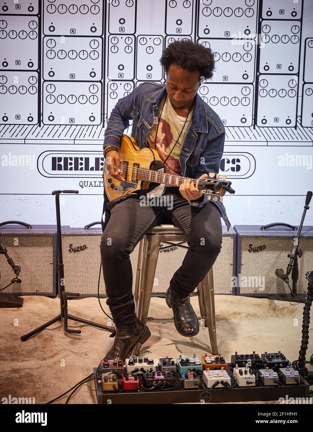 Chitarrista elettrico maschio nero seduto sullo sgabello che suona Keeley Pedali di chitarra al Musical Instrument Convention Foto Stock
