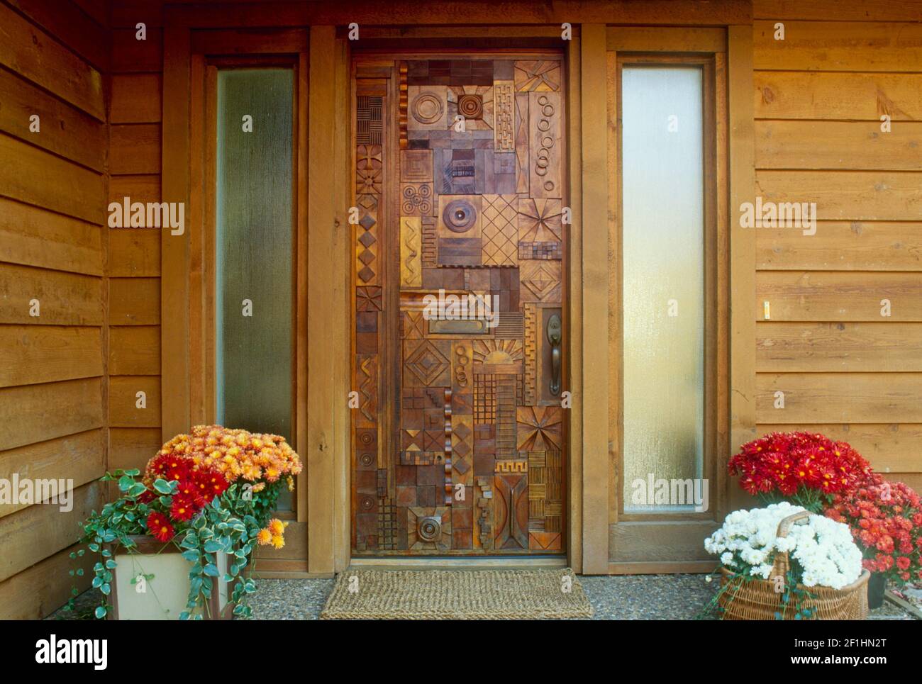 La porta d'ingresso realizzata a mano con disegni geometrici in legno accoglie gli ospiti all'entrata di una casa con fiori in fiore, Missouri, USA Foto Stock