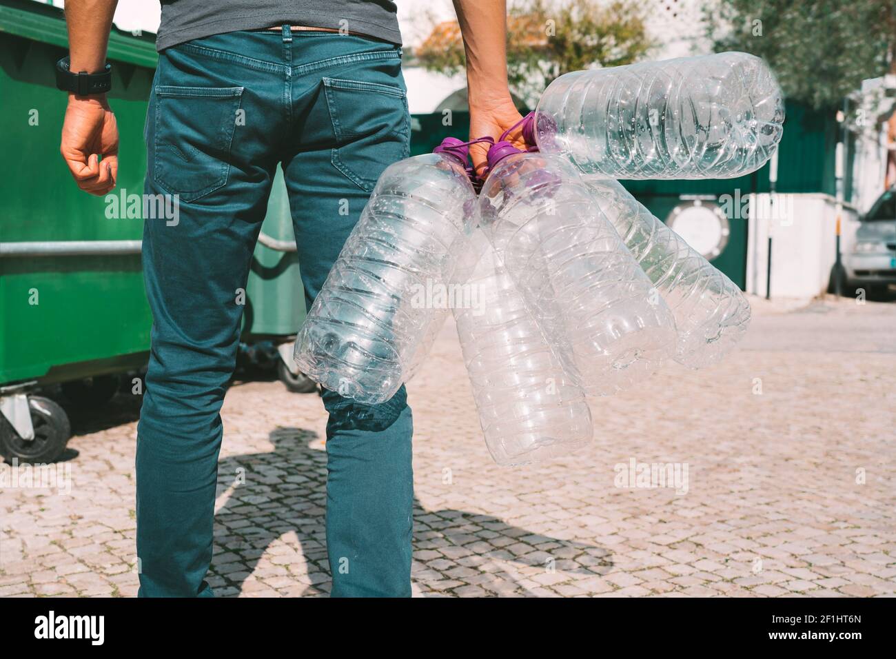 Uomo gettando fuori vuoto usato grandi bottiglie d'acqua di plastica nel contenitore principale dei rifiuti. Bottiglie d'acqua non riciclabili. Problemi di acqua in bottiglia e inquinamento Foto Stock