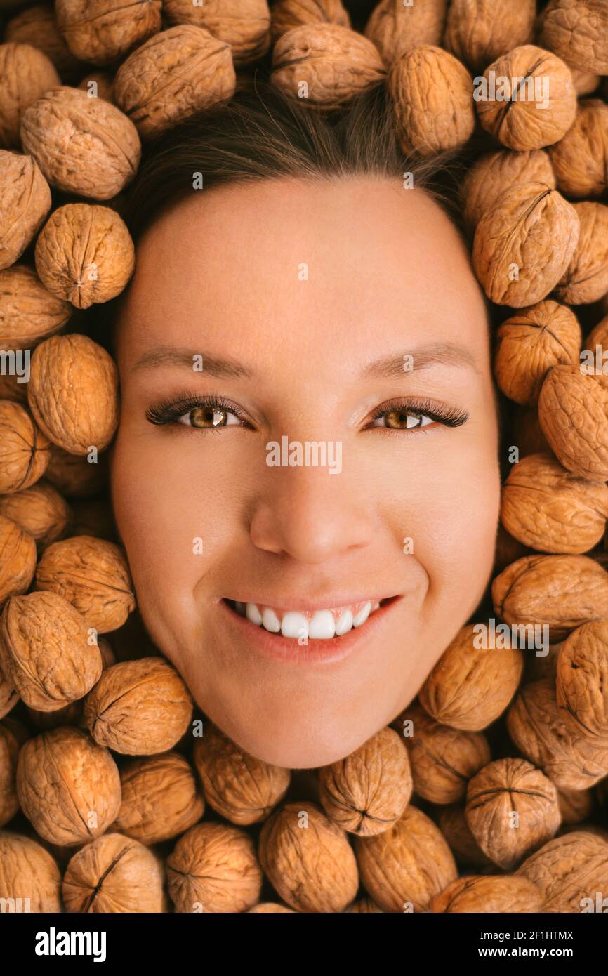 Donna sorridente faccia su sfondo noci. Mangiare noci. Denti forti Foto Stock