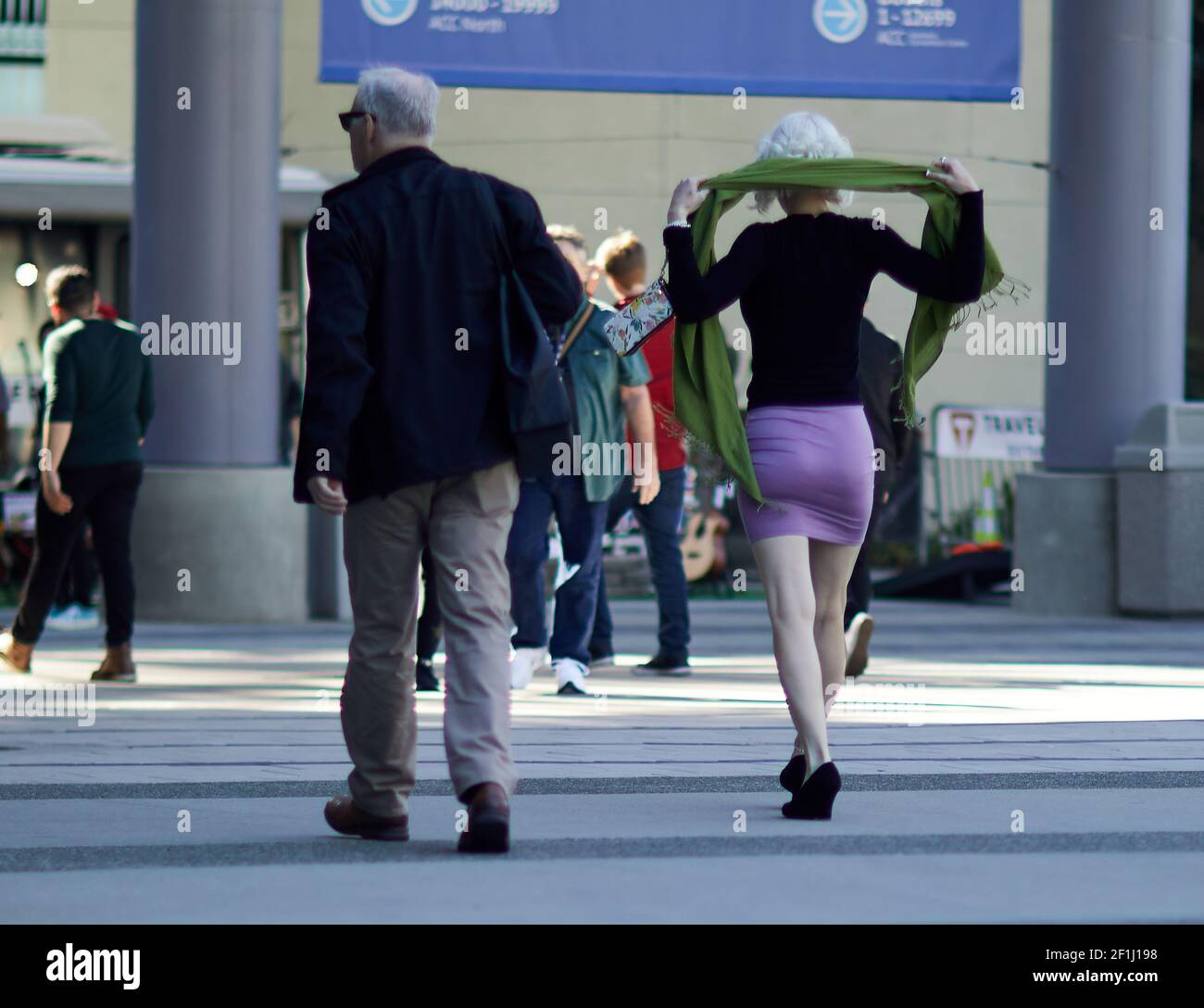 Bella donna in gonna rosa corta e tenente sciarpa verde sopra le spalle camminando nella piazza affollata Foto Stock
