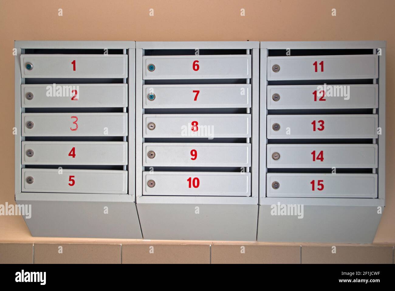 Caselle di posta grigie verniciate con tombini con numeri di appartamento rossi su le porte pendono sulla parete beige dell'entrata foyer all'ingresso di un multi Foto Stock