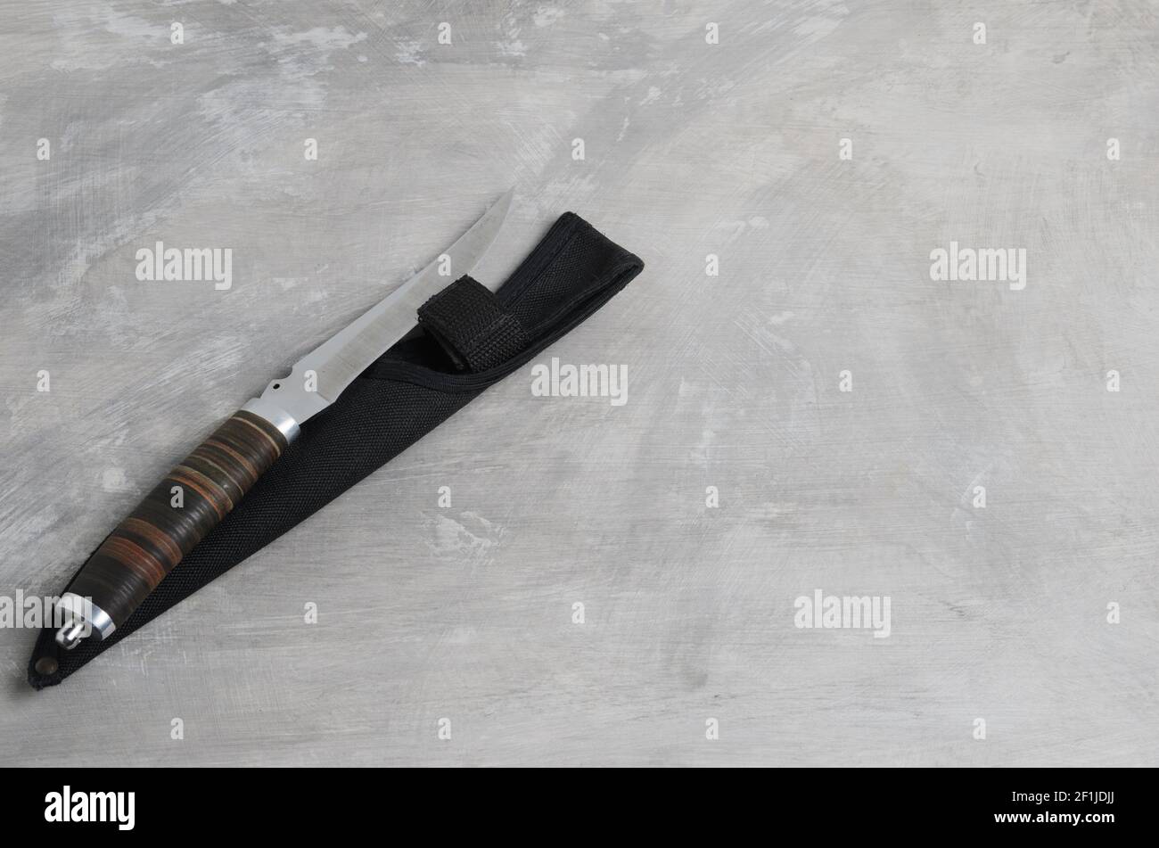 Un elegante coltello da caccia con scabarda e manico in pelle su fondo grigio cemento. Messa a fuoco selettiva. Foto Stock