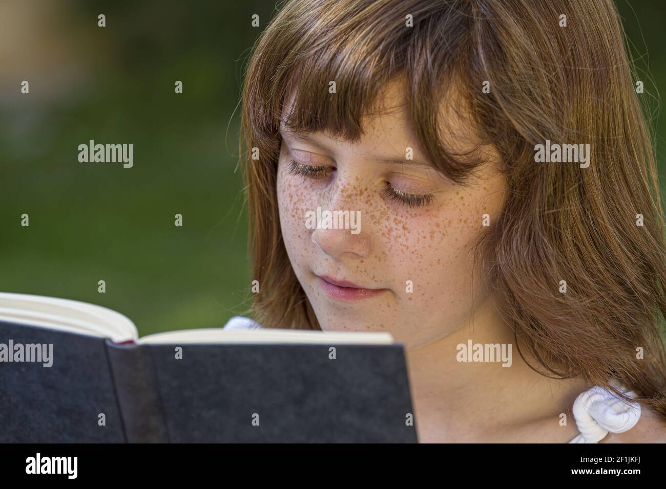 Ragazza rossa che legge un libro in un parco con bella erba verde, natura e vita sana Foto Stock