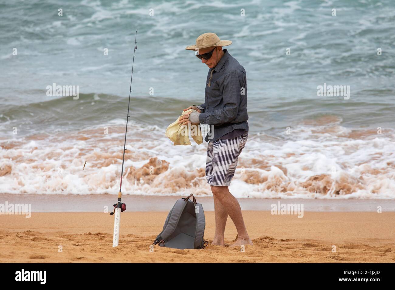 Pesca in spiaggia, uomo anziano pesca in mare su una spiaggia di Sydney in  Australia indossare pantaloncini e un cappello Foto stock - Alamy