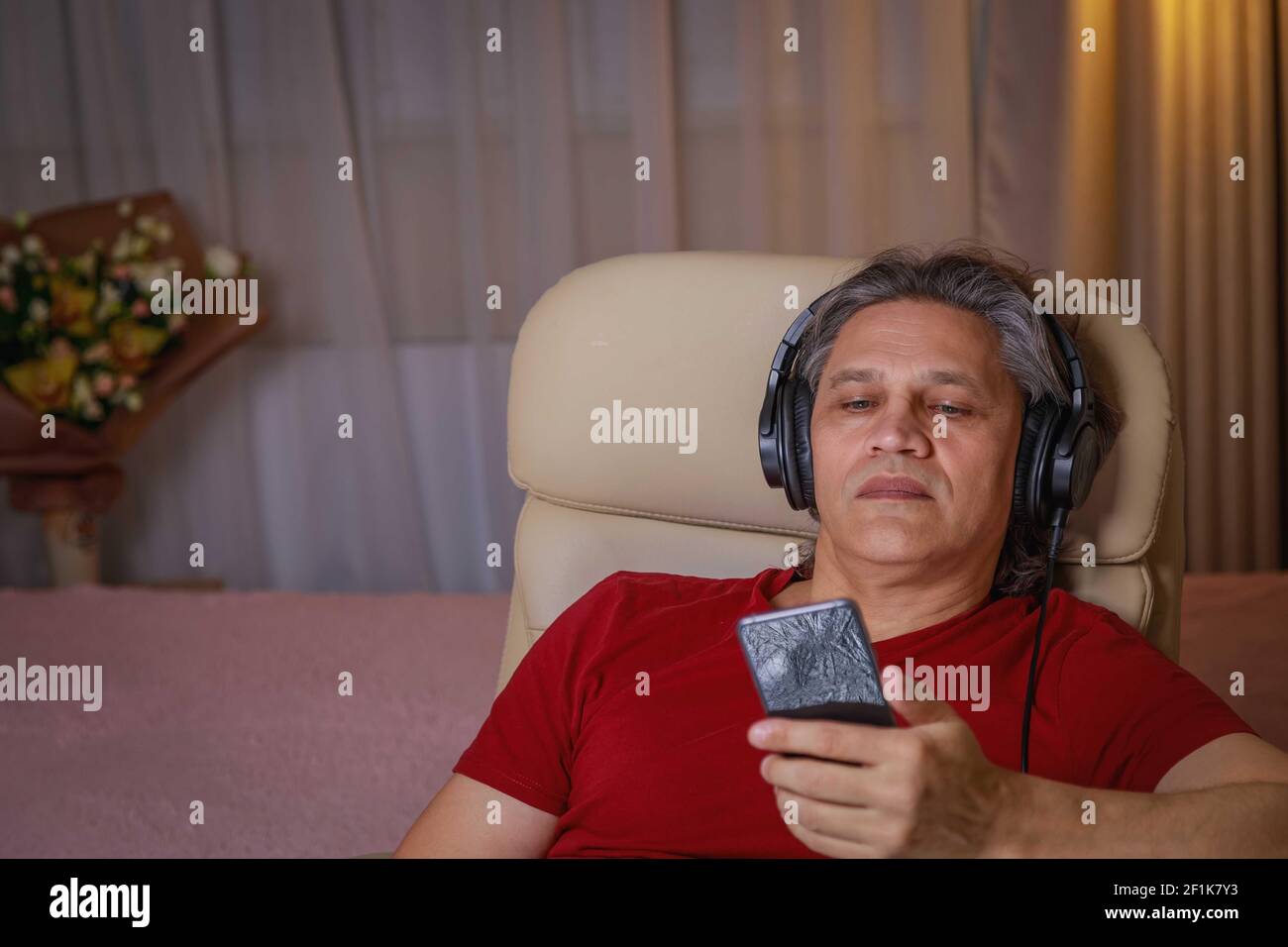 un uomo di 50 anni ascolta la musica con le cuffie a casa, seduto su una sedia. Delizia rilassante. Foto Stock