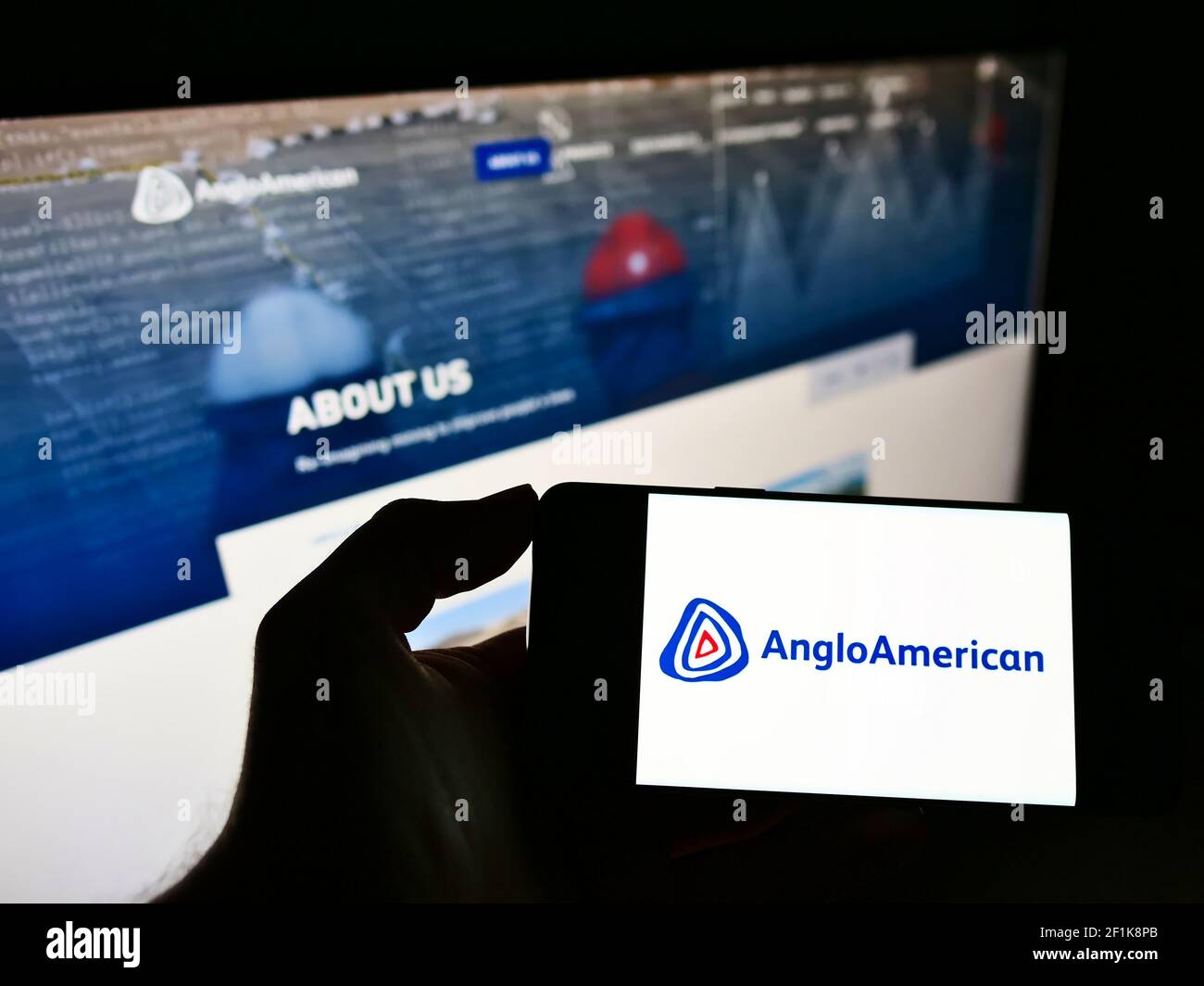 Persona che detiene smartphone con logo di metalli globali e società mineraria Anglo American plc sullo schermo di fronte al sito web. Mettere a fuoco il display del telefono. Foto Stock