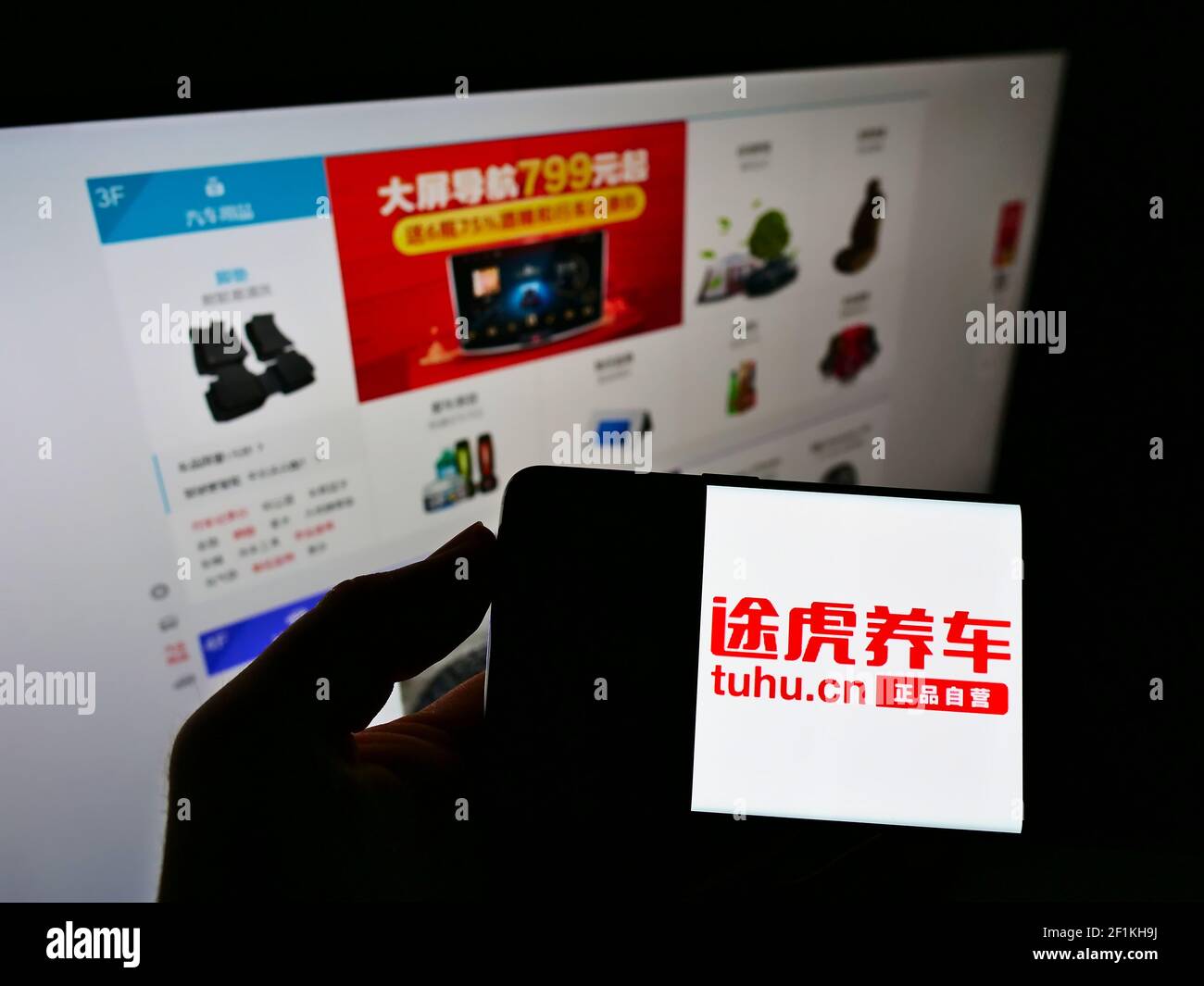 Persona che tiene il telefono mobile con il logo della società cinese di parti automobilistiche Tuhu sullo schermo di fronte al sito web con negozio web. Mettere a fuoco il display del telefono. Foto Stock