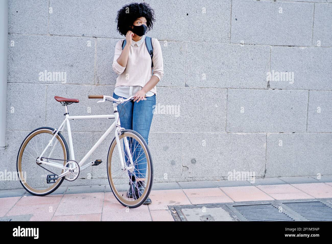Donna afroamericana con uno smartphone in mano. Donna con maschera protettiva. Andare in bicicletta in città. Foto di alta qualità Foto Stock