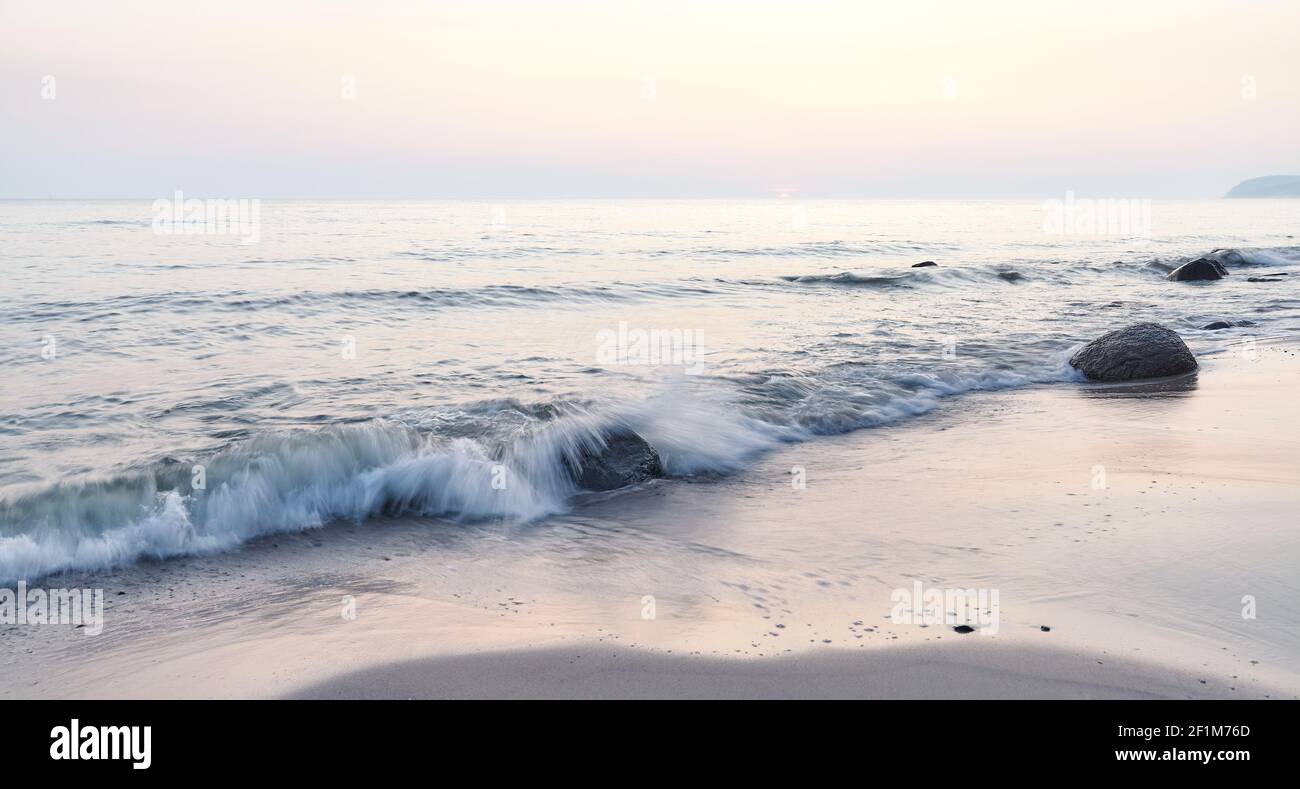 Alba tranquilla su una spiaggia, fuoco su rocce, foto di esposizione lunga. Foto Stock