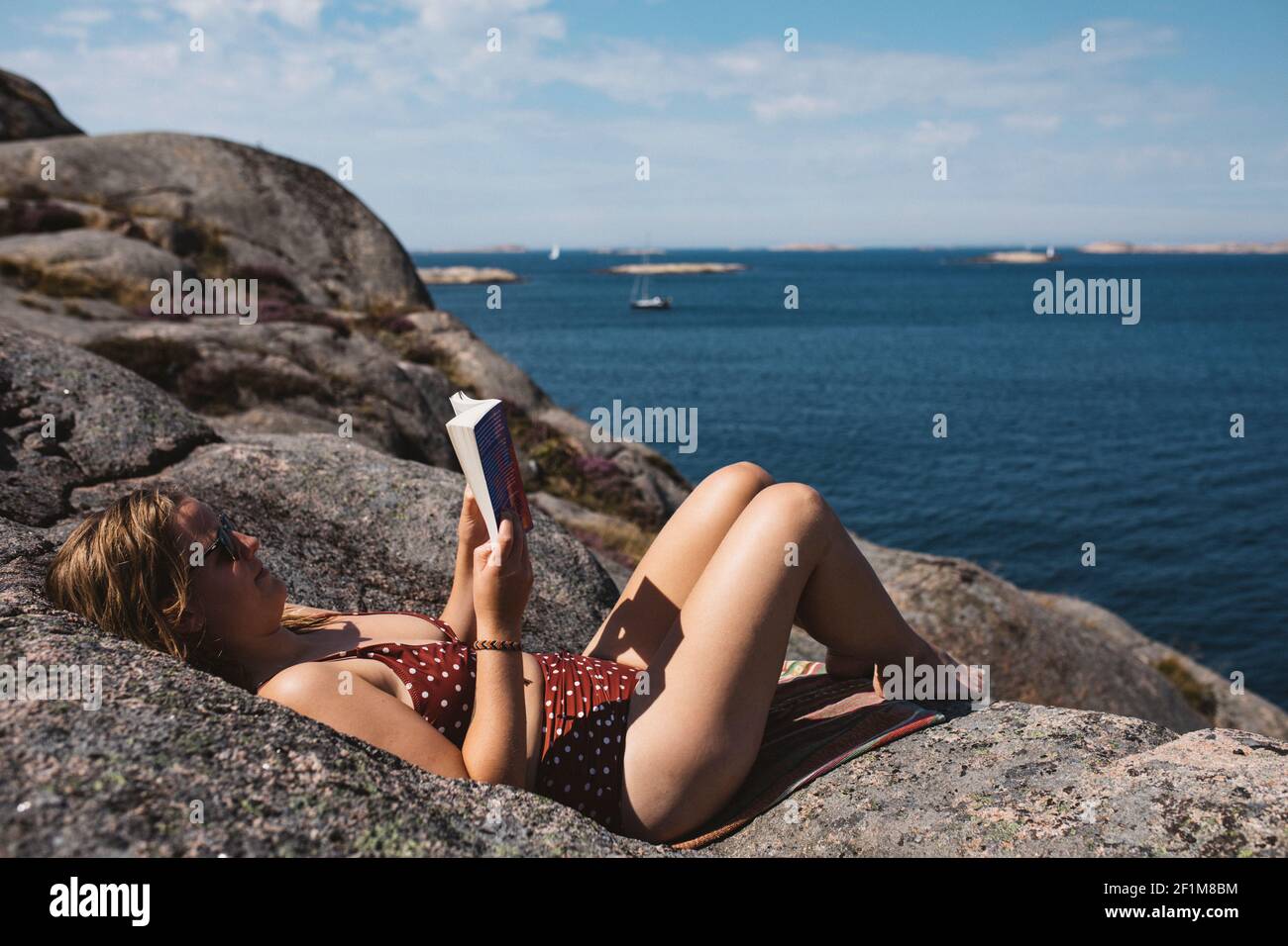 Donna che legge libro sulla costa rocciosa Foto Stock
