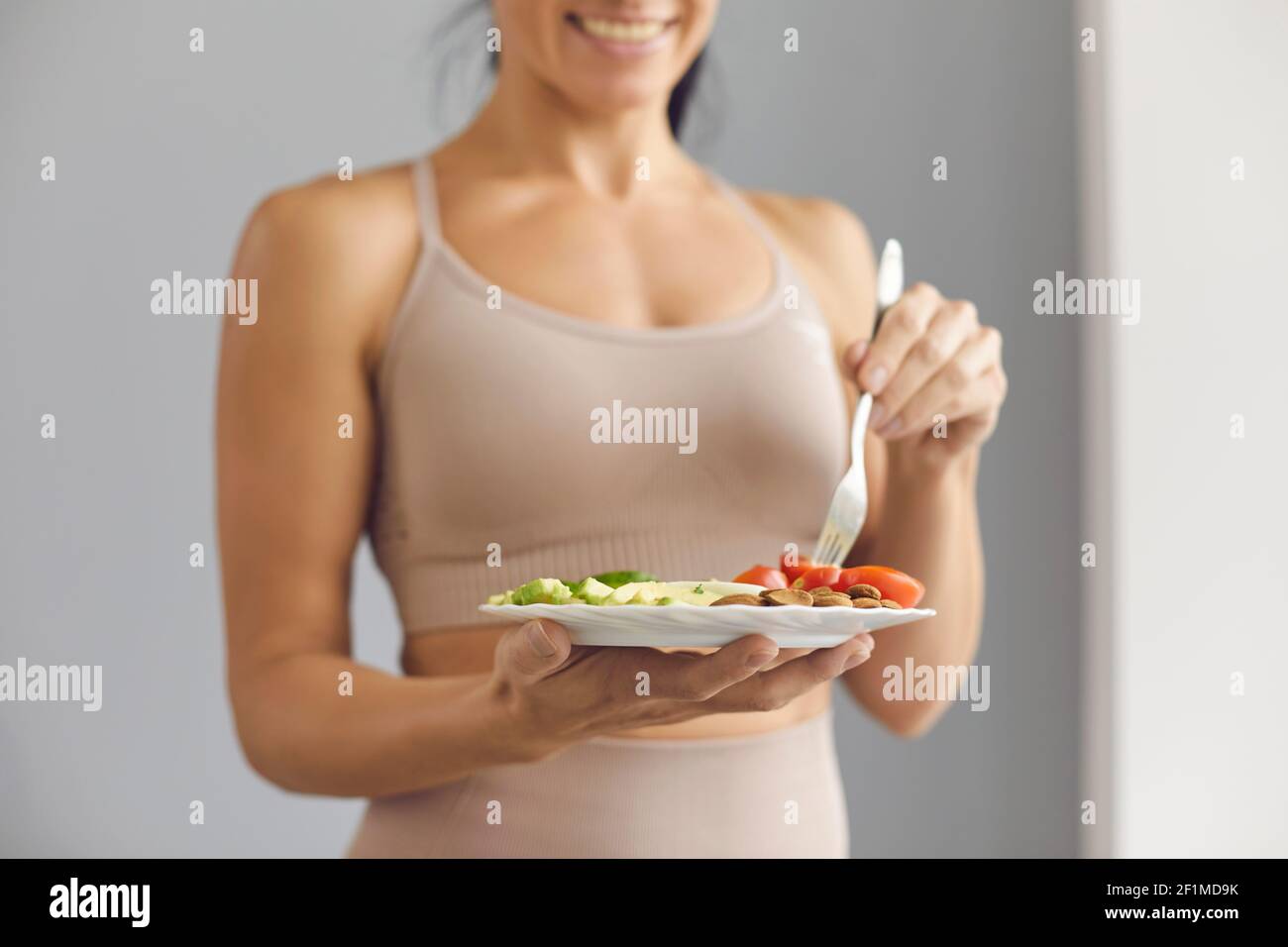 Donna felice in forma sorridente, tenendo un piatto e gustando il suo sano pasto vegetariano Foto Stock