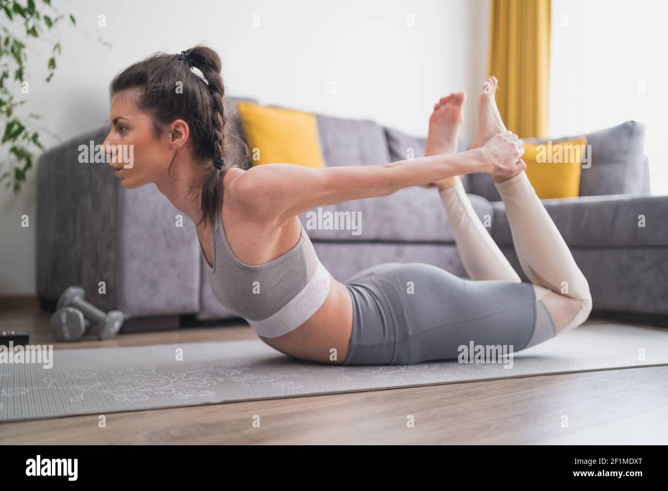 Giovane bella donna che pratica yoga, sdraiata in Bow posa sul tappeto yoga a casa Foto Stock
