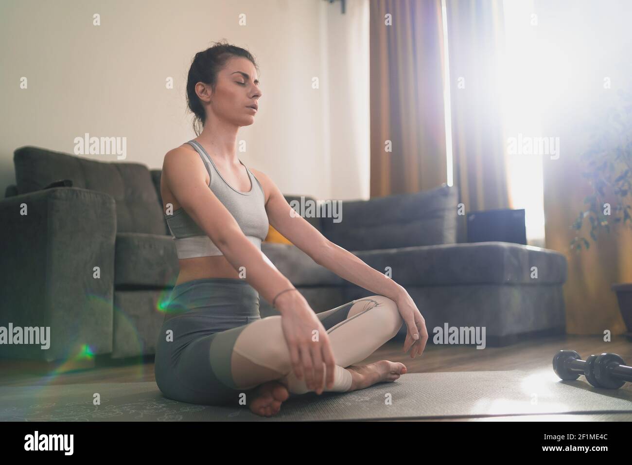 Calma bella giovane donna meditando con gli occhi chiusi seduta sopra tappetino yoga Foto Stock
