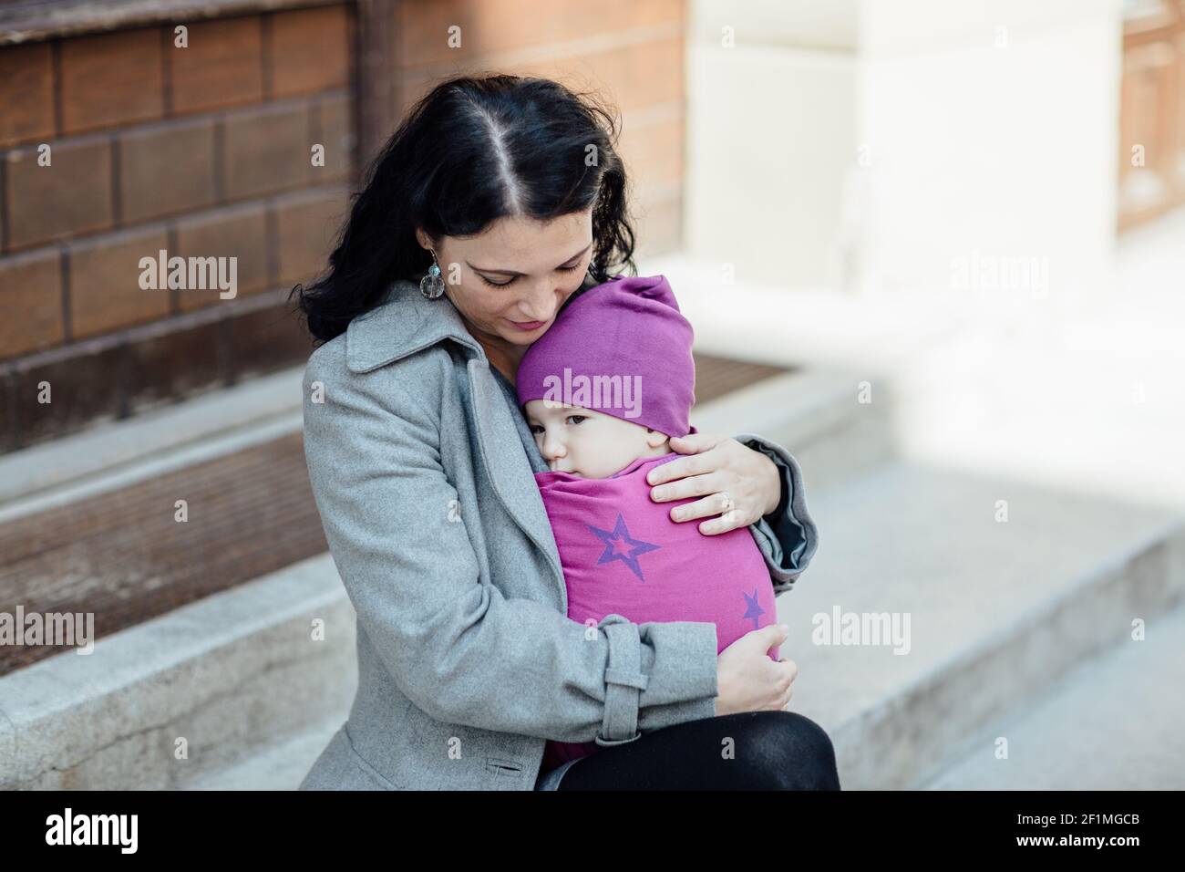 Ritratto della madre di babyweing trendy che porta il suo bambino nel città Foto Stock