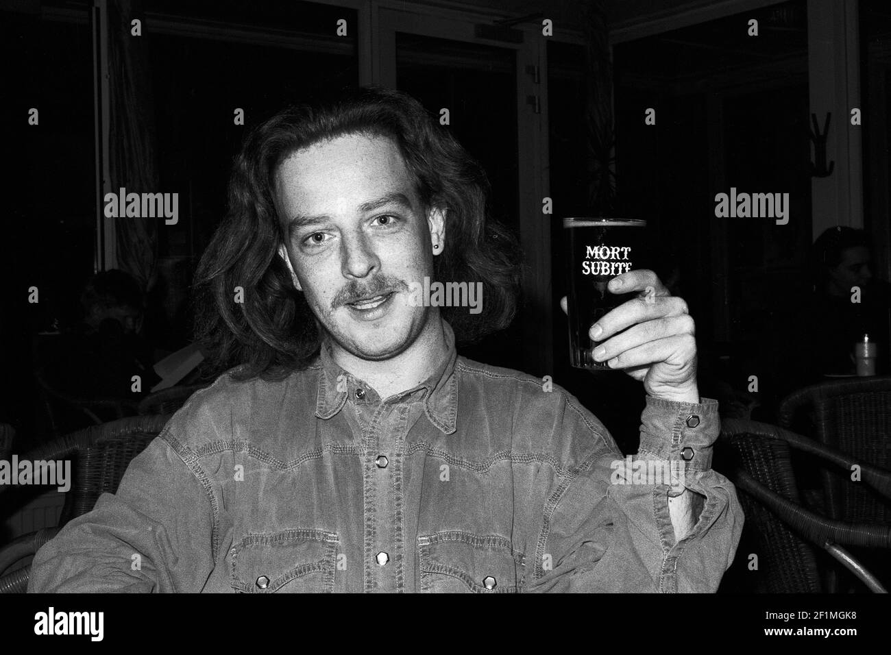 Tilburg, Paesi Bassi. Ritratto di un giovane adulto dai capelli lunghi che beve una birra artigianale Mort Subite. Foto Stock