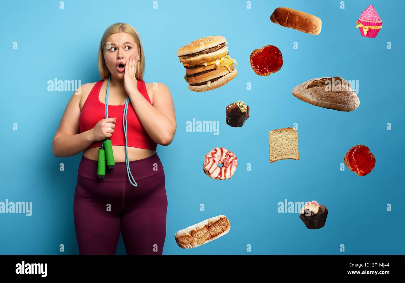 Fat ragazza fa palestra, ma lei pensa sempre al cibo. Sfondo ciano Foto Stock