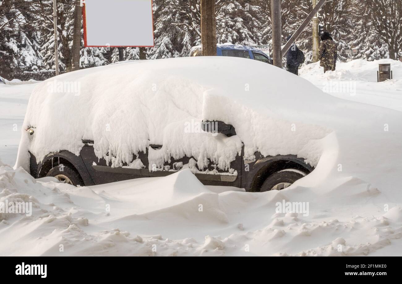 Città strada dopo Blizzard. Automobili bloccate sotto la neve e il ghiaccio. Veicolo sepolto in una deriva da neve sulla strada. Parcheggio in inverno dopo una nevicata pesante Foto Stock