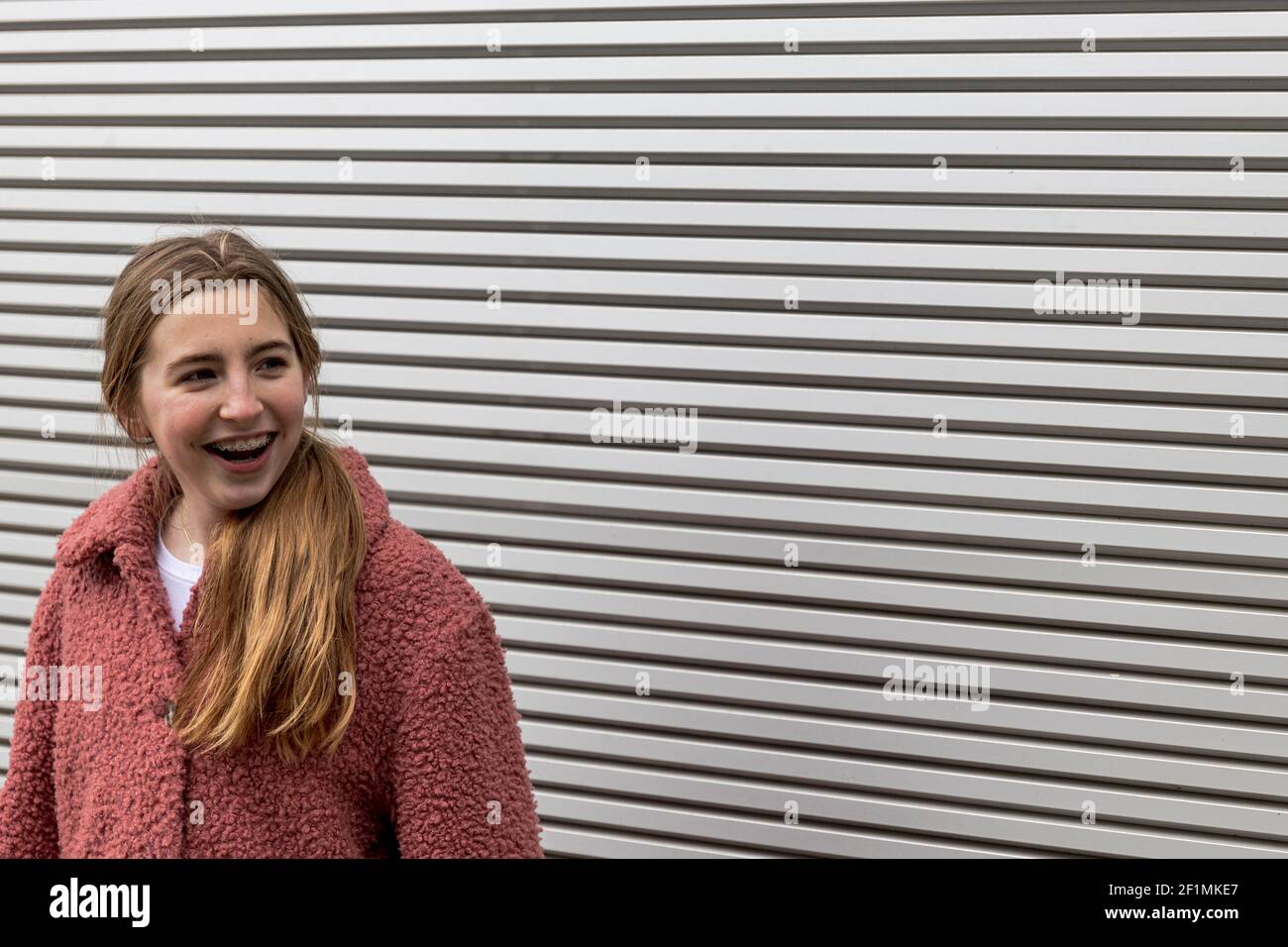 Bionda ragazza con bretelle sorridenti di fronte a una striscia sfondo Foto Stock