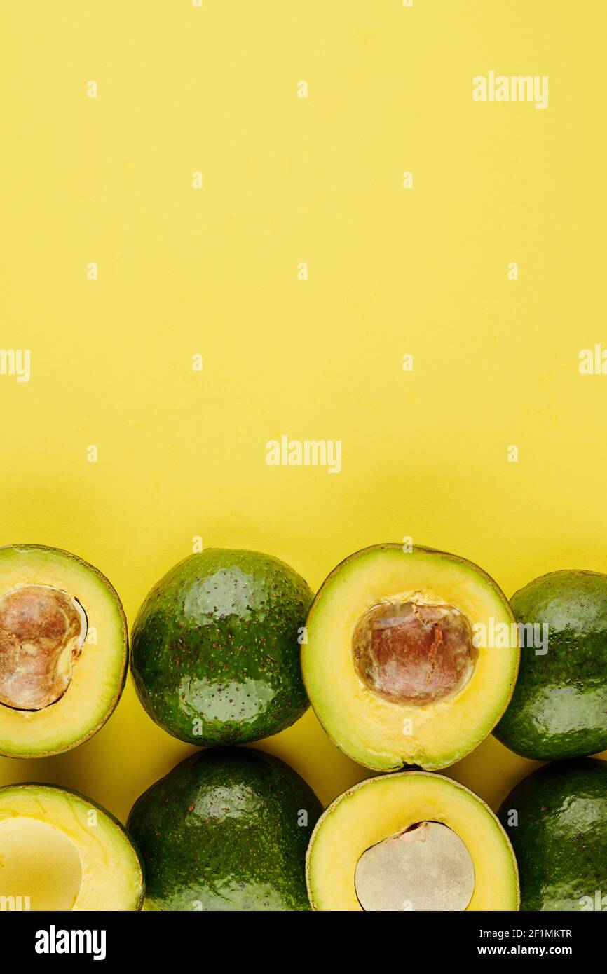 Sfondo giallo con avocado intero e tagliato, cibo sano e concetto di nutrizione Foto Stock