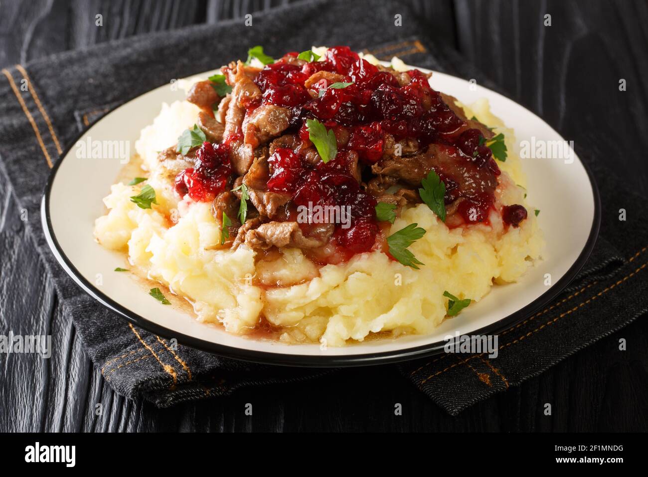 Porzione di veleno fatto in casa con purè di patate e salsa di lingonberry primo piano in un piatto sul tavolo. Orizzontale Foto Stock