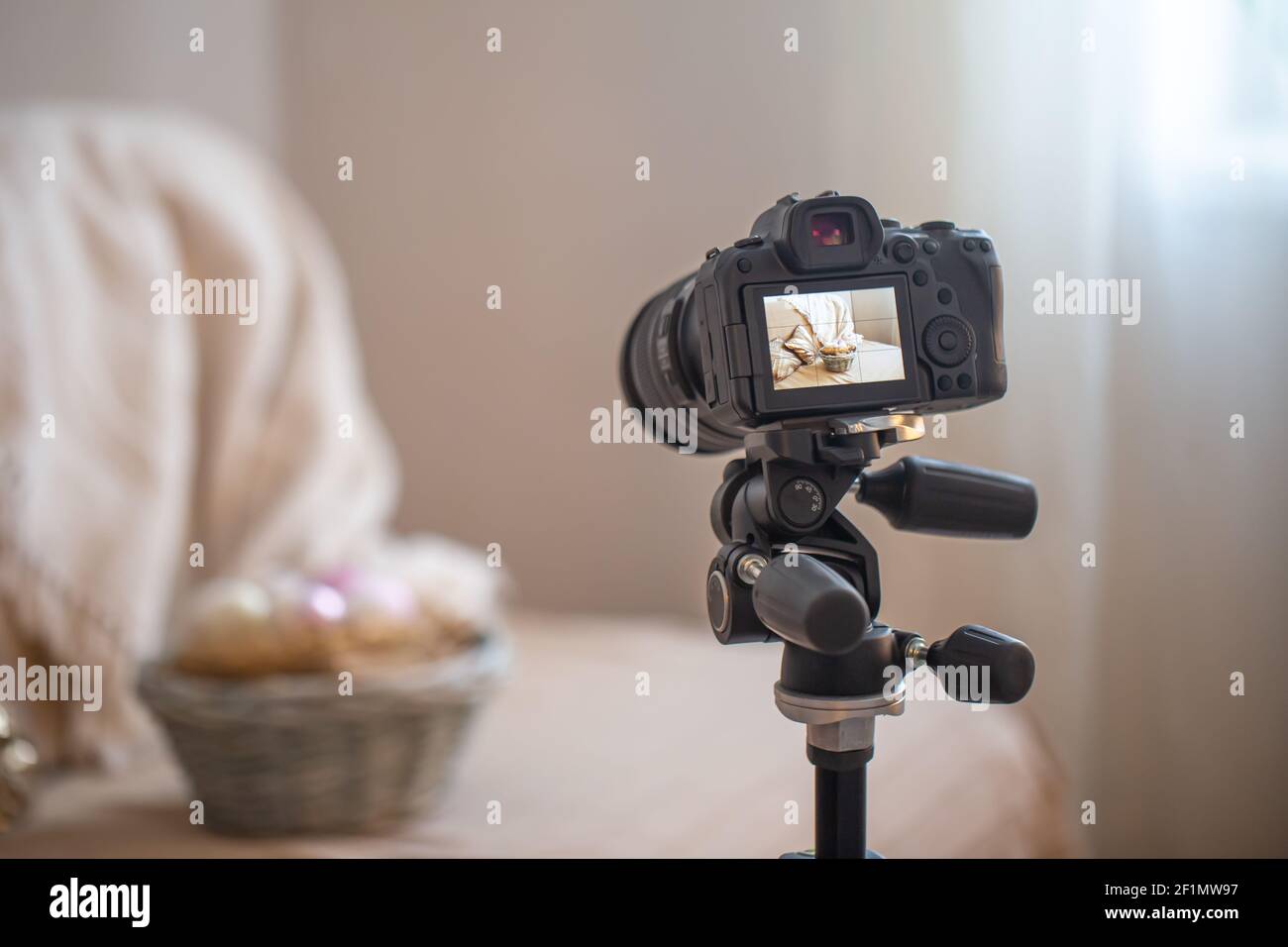 Primo piano di una fotocamera digitale professionale su un treppiede mentre si scatta una composizione domestica su sfondo sfocato. Foto Stock