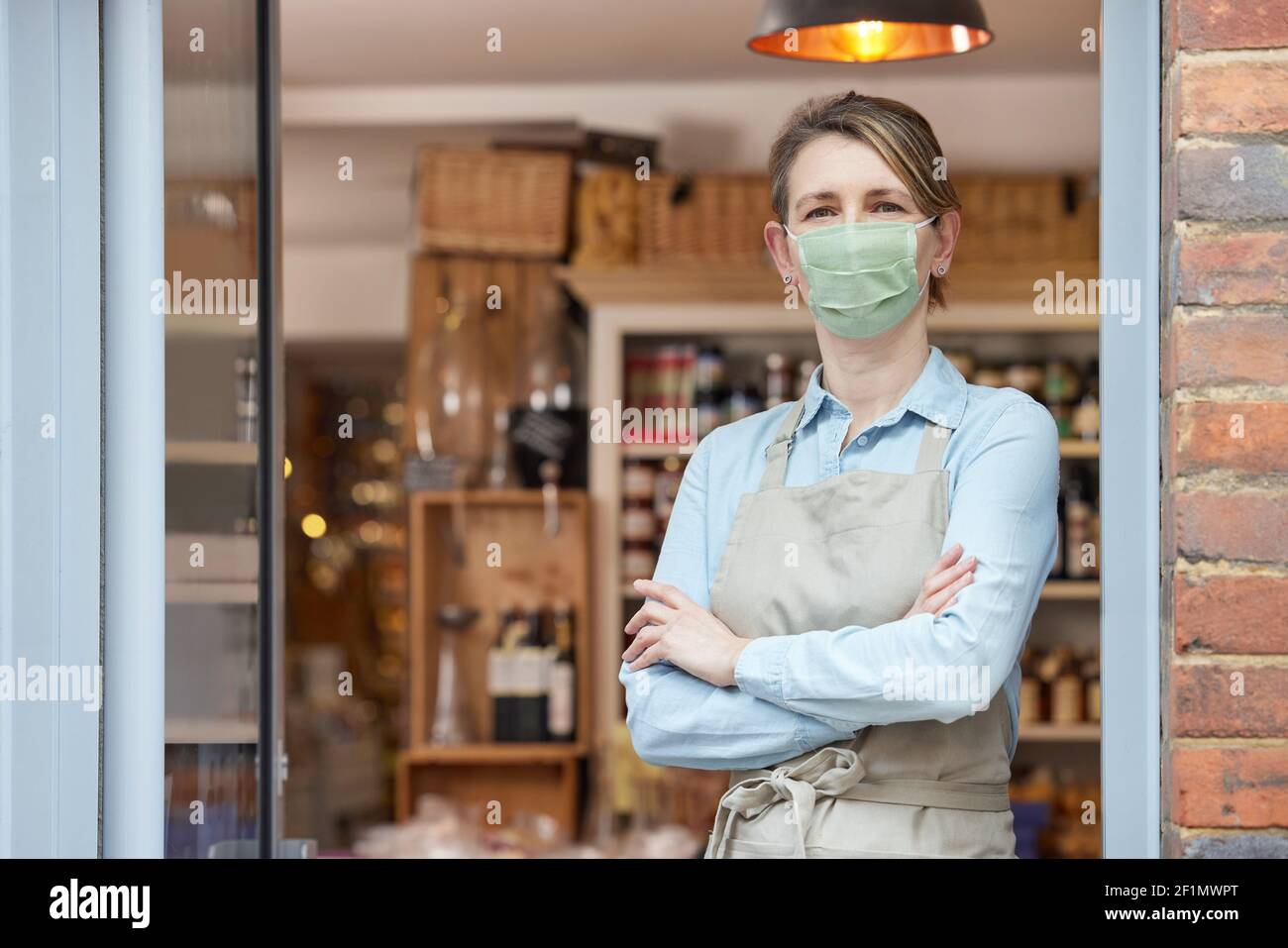 Ritratto del proprietario femminile in piedi fuori Delicatessen indossare maschera facciale Durante la Pandemia di salute Foto Stock