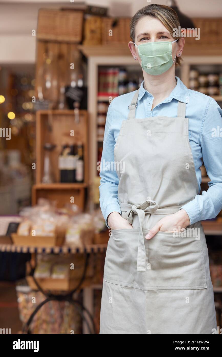 Ritratto del proprietario femminile in piedi fuori Delicatessen indossare maschera facciale Durante la Pandemia di salute Foto Stock