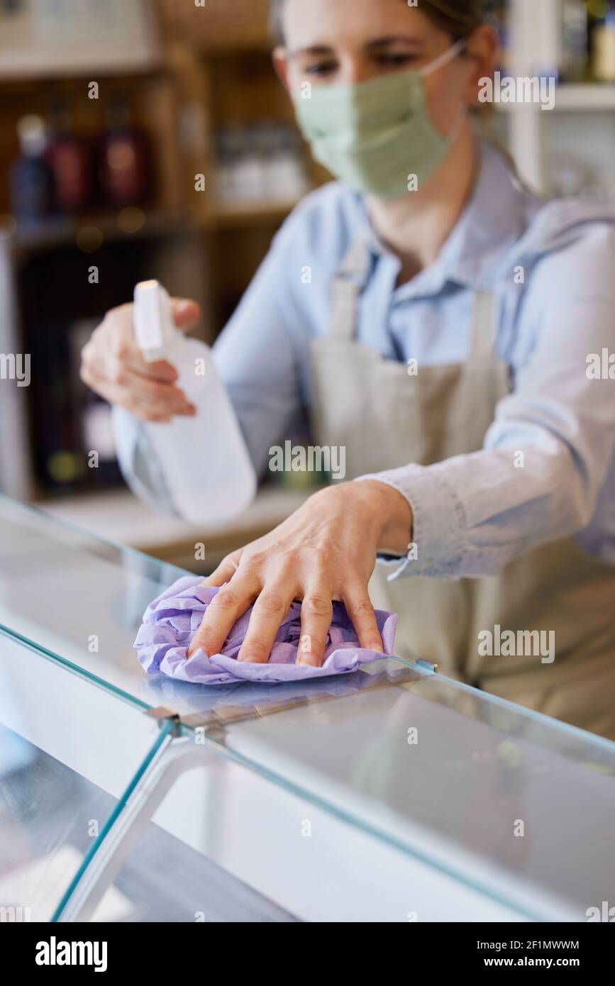 Donna Proprietario Dicatessen indossare maschera viso contatore di pulizia con disinfettante Spray Foto Stock
