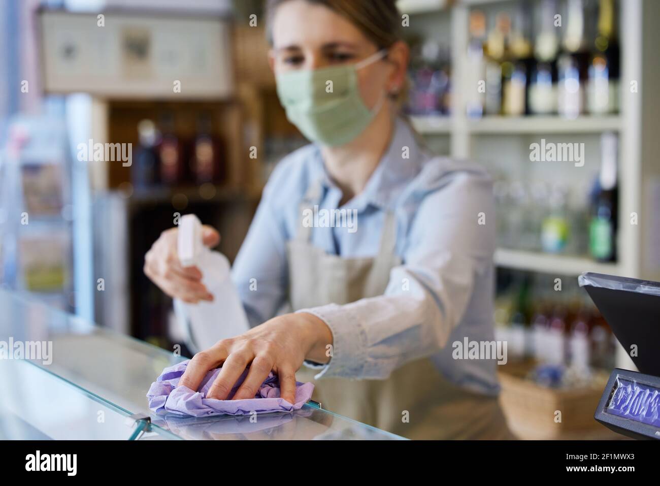 Donna Proprietario Dicatessen indossare maschera viso contatore di pulizia con disinfettante Spray Foto Stock