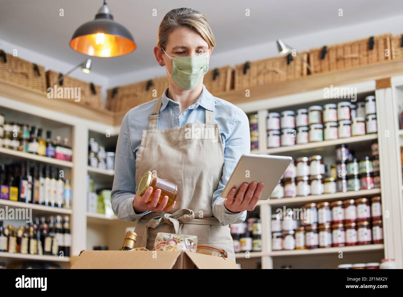 Donna Proprietario Delicatessen con Tablet digitale indossare maschera di preparazione Ordine di alimentari online Foto Stock