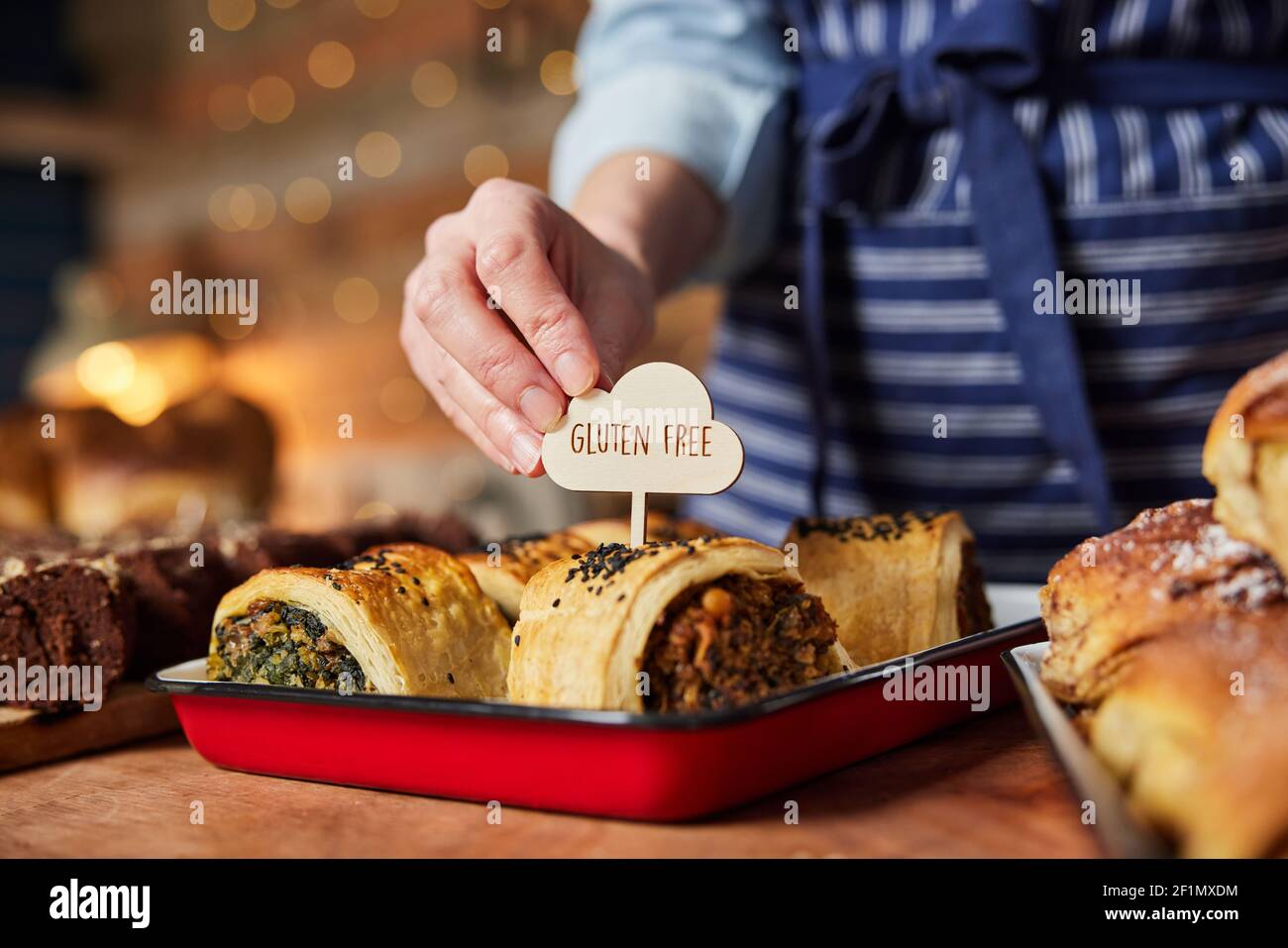 Assistente vendite in panetteria che mette l'etichetta senza glutine in fresco Rotolo di salato al forno Foto Stock