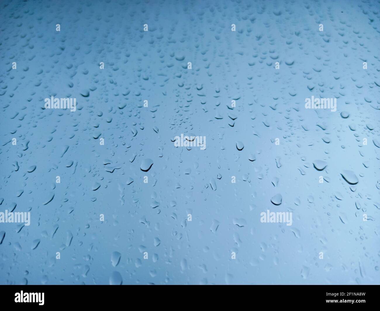 Gocce di pioggia su un primo piano del riquadro della finestra. Sfondo blu astratto. Foto Stock