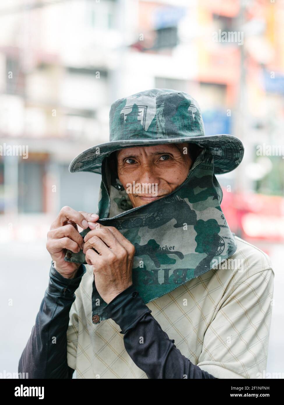 Primo piano di un operaio asiatico che indossa un grande cappello e una copertura facciale come protezione dal sole che splazia, Bangkok Thailandia. Foto Stock