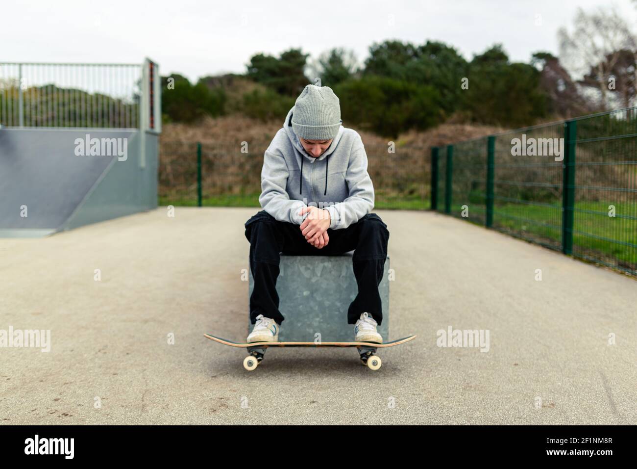 Ritratto di un giovane adulto maschio con uno skateboard seduto su una scatola in uno skatepark locale. Skateboard concetto di stile di vita sano Foto Stock