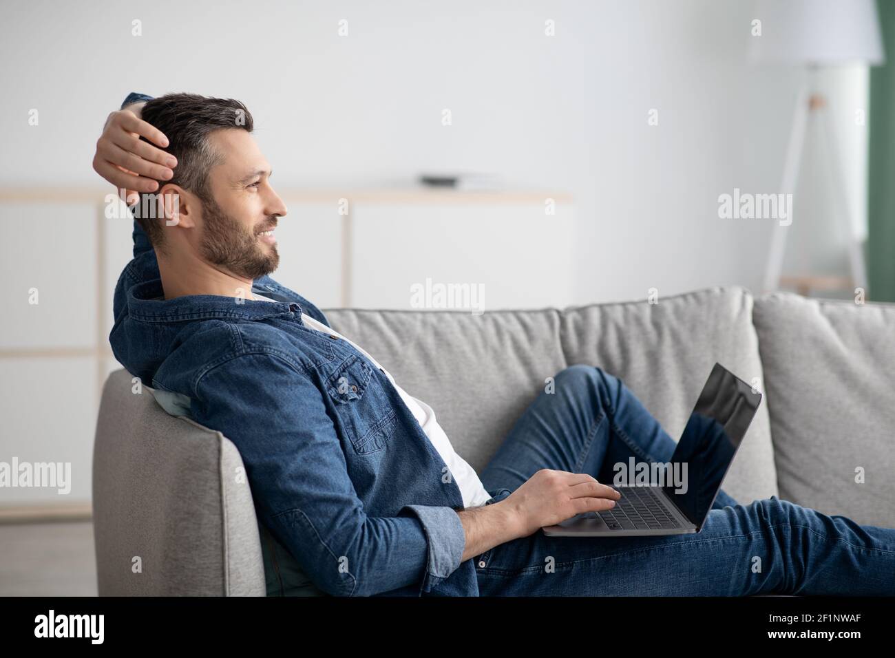 Felice uomo di mezza età in posa casual sul divano a casa, utilizzando il computer portatile, guardando film, spazio per la copia. Bell'uomo bearded leggere blog o giocare giochi Foto Stock