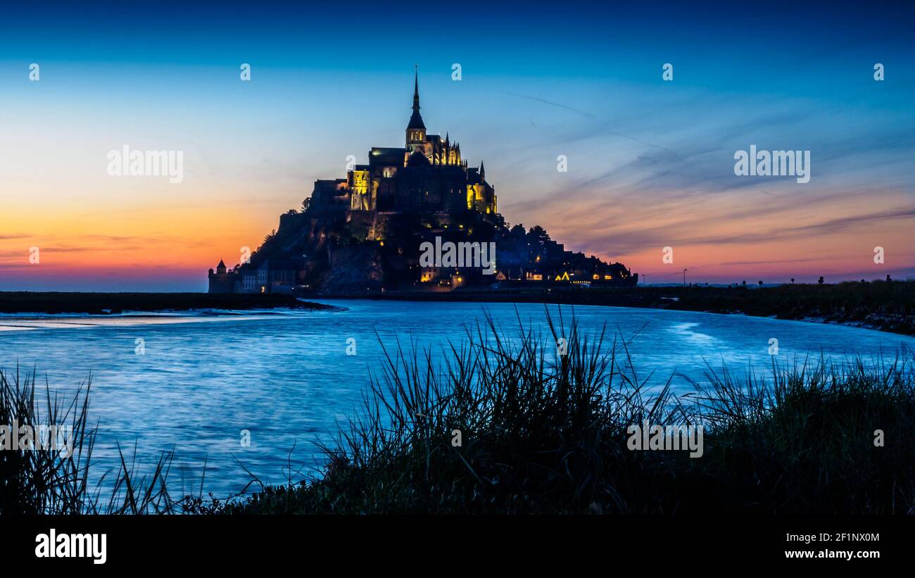 La luce della sera tarda dona al cielo un'illuminazione rosea Mont St Michel in Normandia Francia Foto Stock
