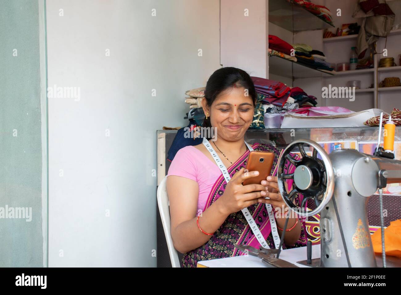 donna indiana su misura che tiene il telefono cellulare in officina Foto Stock