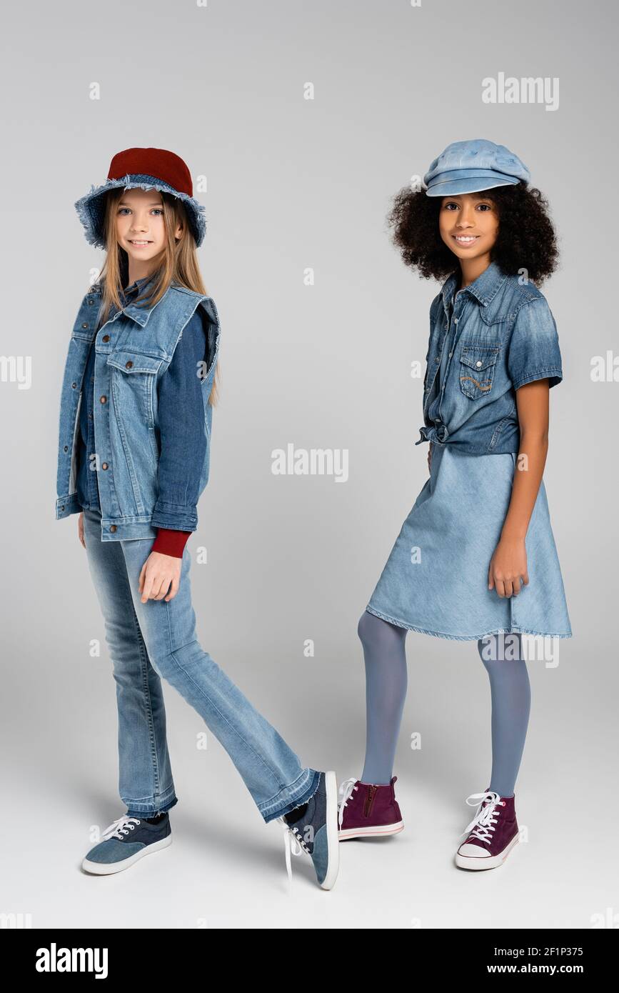 due ragazze interrazziali in jeans alla moda e cappelli in posa su grigio  Foto stock - Alamy