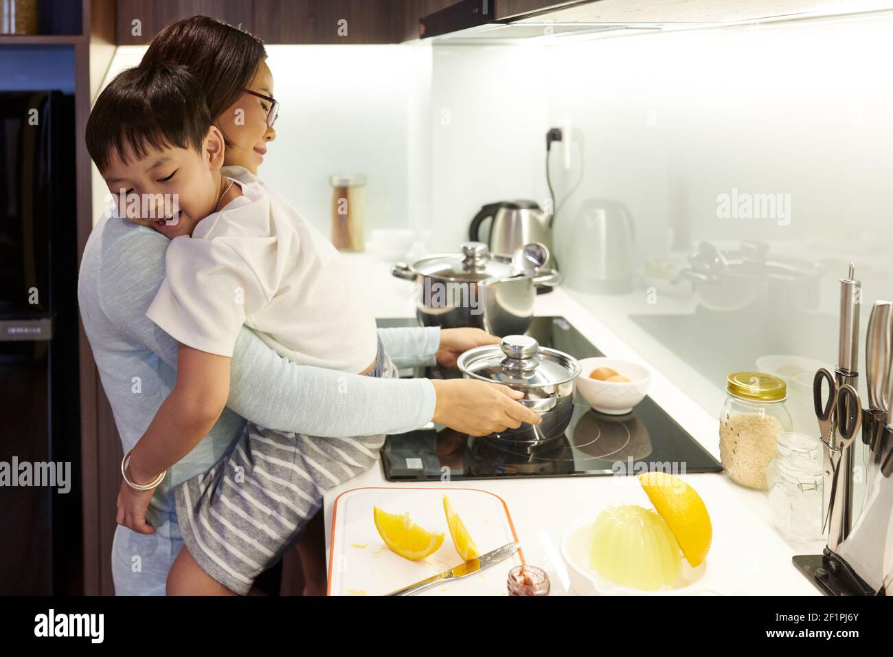 Madre abbracciando suo figlio e mettendo pentola con acqua sopra piano cottura Foto Stock