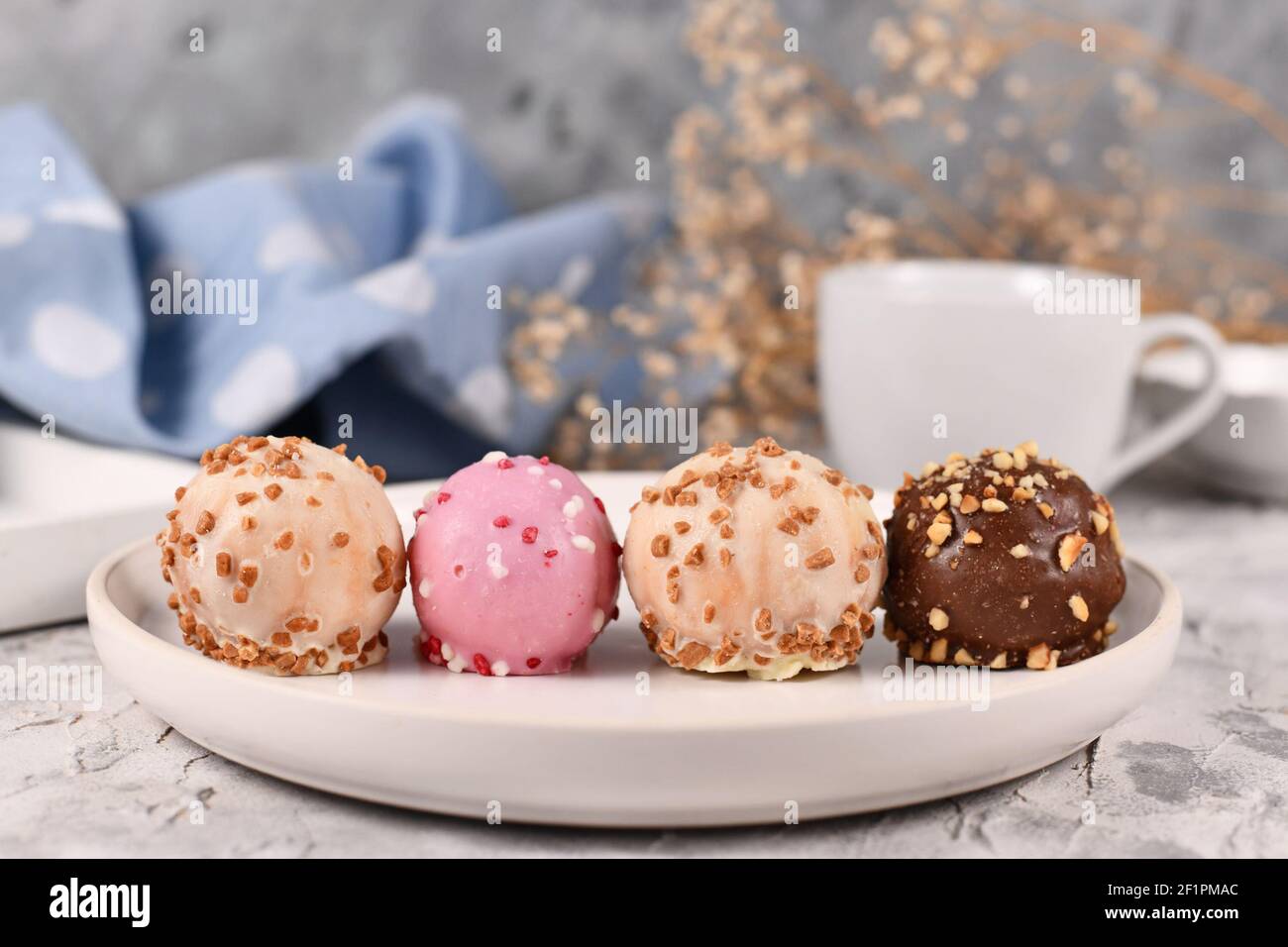 Piccole palline colorate smaltate con cioccolato bianco, rosa e marrone con spruzzini in fila su piatto bianco Foto Stock