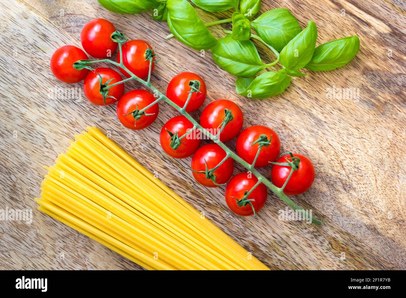 Pomodori maturi circondati da foglie di basilico fresco e spaghetti secchi su una tavola di legno Foto Stock