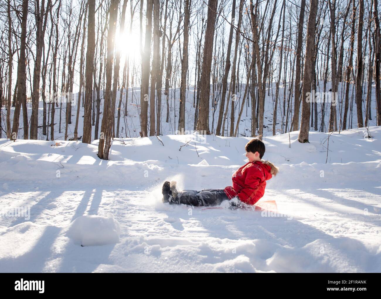 Un bambino che dorme giù su una collina innevata in una zona boscosa durante il giorno di sole. Foto Stock