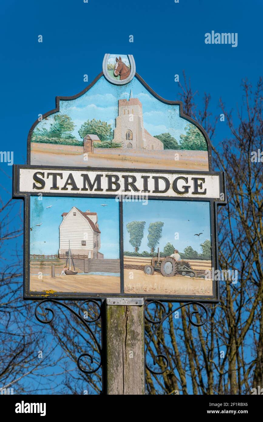 Segno del villaggio di Stambridge con immagini di caratteristiche locali, tra cui la chiesa di Santa Maria e tutti i Santi, trattore che coltivano un campo e un mulino Foto Stock