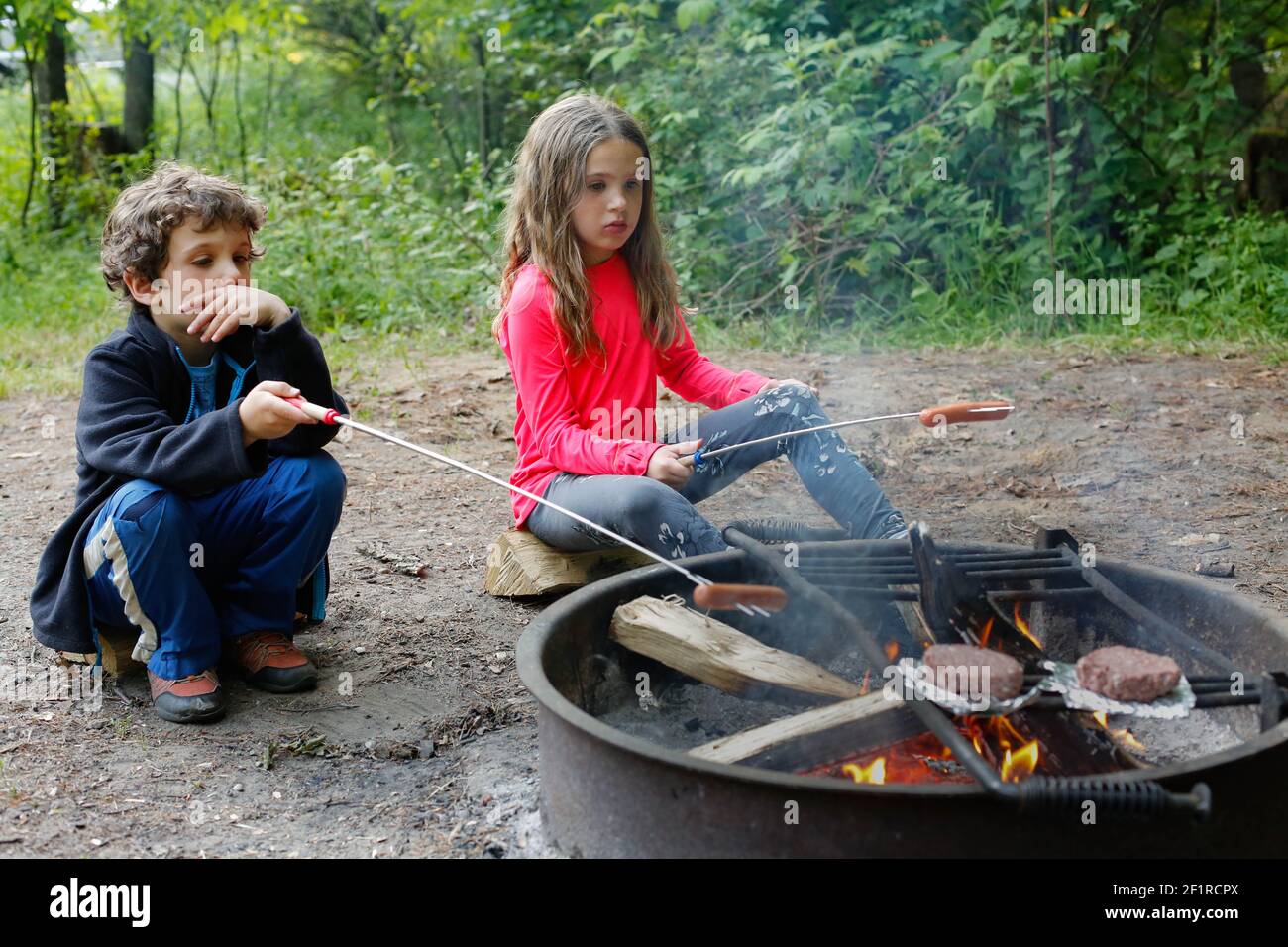 Due bambini che tostano hot dogs mentre campeggiano Foto Stock