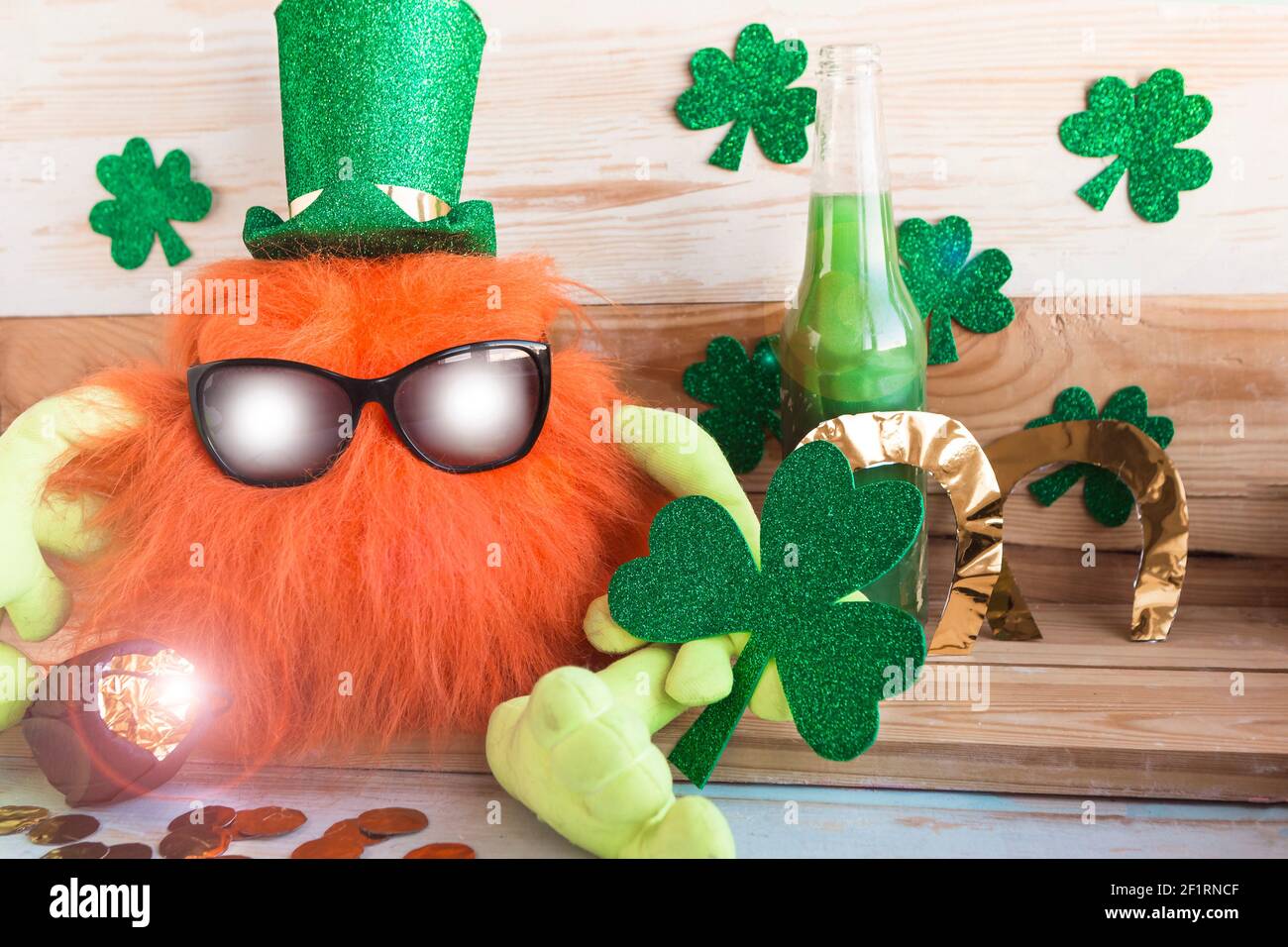 Il leprechaun giocattolo con la barba di zenzero in cappello verde e gli occhiali da sole tiene uno shamrock nelle sue mani. Il concetto di celebrazione del giorno di San Patrizio Foto Stock