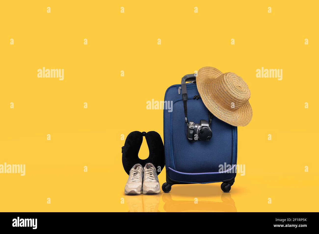 Bagaglio a mano con ruote blu e oggetti da viaggio essenziali su sfondo giallo. Foto Stock