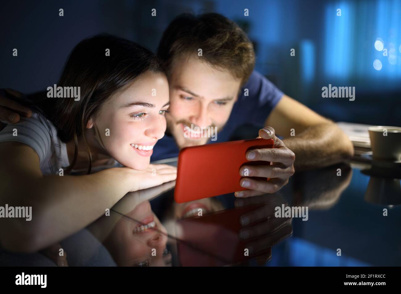 Felice coppia che guarda i contenuti multimediali sul telefono cellulare orizzontale in la notte a casa Foto Stock